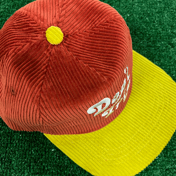 Don't Trip red and yellow corduroy hat with white embroidered Don't Trip logo on grass background - Free & Easy