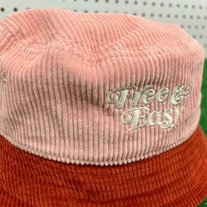 Free & Easy Don't Trip pink and red corduroy bucket hat with white embroidered logo on grass background - Free & Easy