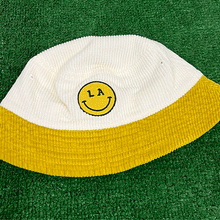Load image into Gallery viewer, LA Be Happy smiley face embroidered on white corduroy yellow brim bucket hat on grass background - Free &amp; Easy
