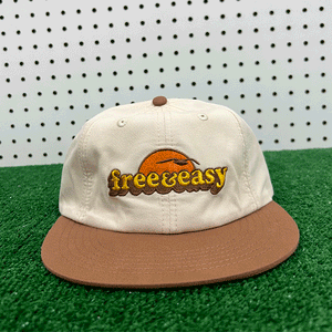 Free & Easy bone and brown lightweight hat with orange, yellow and brown embroidered sun with bird logo on grass background - Free & Easy